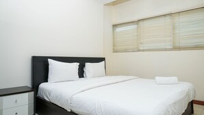 Una cama bien hecha con sábanas blancas, cabecera oscura y mesita de noche blanca con cajones.