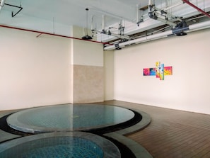 A room with two circular pools, a tiled floor, and a wall with three colorful paintings.