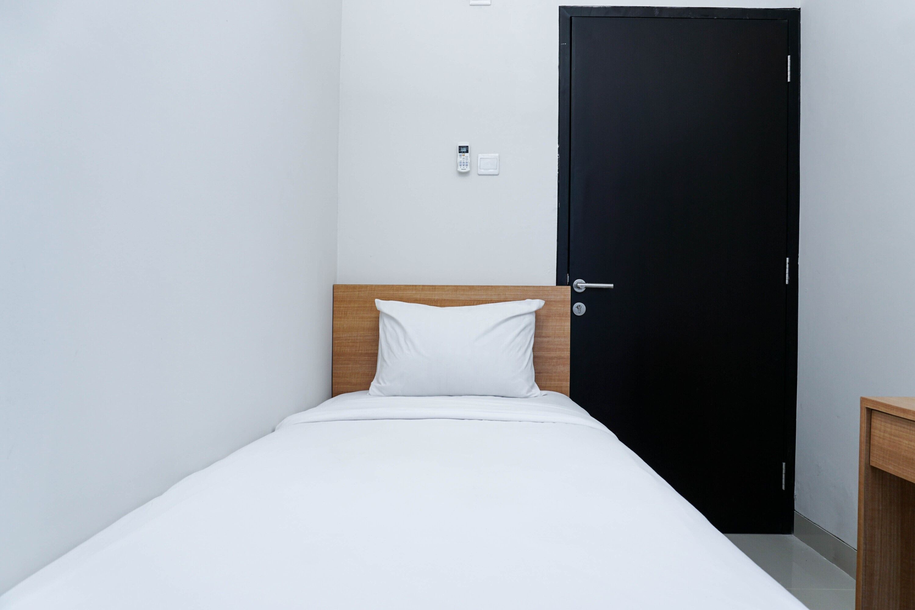 Una cama individual con ropa de cama blanca, un cabecero de madera, una puerta negra y una mesita de noche pequeña.