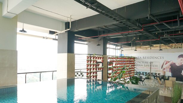 An indoor swimming pool with a tiled floor, surrounded by walls with potted plants, and a banner advertising a modern lifestyle.