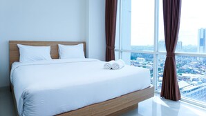 A modern hotel room with a large bed, white linens, and a city view through floor-to-ceiling windows.