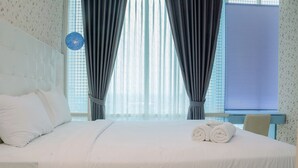 Een hotelkamer met een groot bed, witte beddengoed, een hoofdeinde en een raam met gordijnen.
