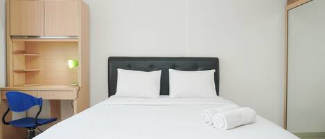 A neatly arranged hotel room with a bed, a desk with a chair, and a wardrobe.