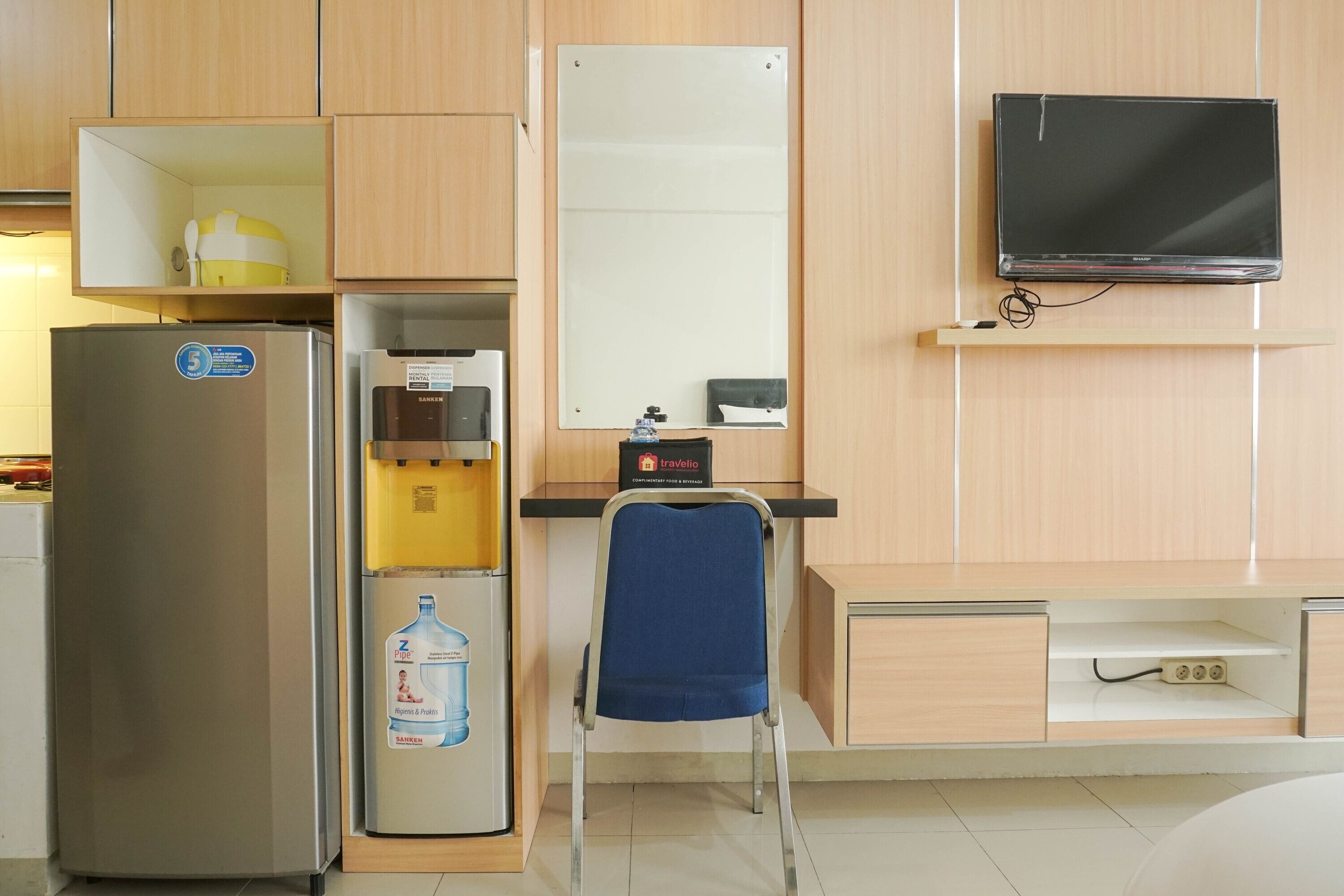 Ein kompaktes Hotelzimmer mit Küchenzeile, einem Flachbildfernseher, einem blauen Stuhl und einem Wasserspender.