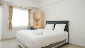 Una cama bien hecha con ropa blanca, un armario de madera y un escritorio con una silla.