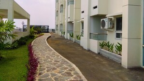 A pathway leading to a modern building with multiple floors, air conditioning units, and potted plants. - Enjoy 1BR Apartment at Atlanta Residence (Depok)