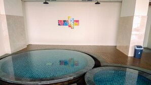 A swimming pool area with three circular pools, wooden flooring, and a wall with colorful artwork. - Enjoy 1BR Apartment at Atlanta Residence (Depok)