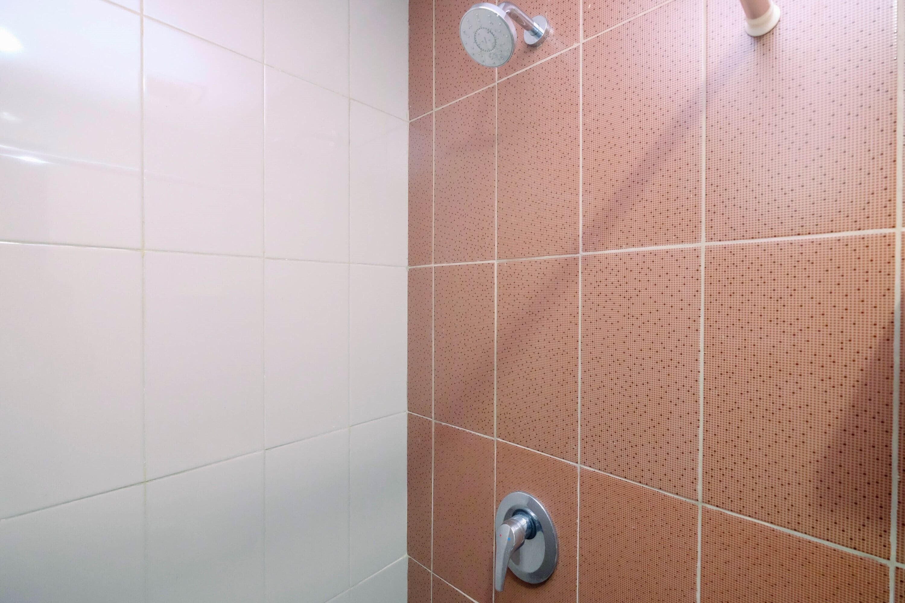 A bathroom with white and pink tiled walls, a shower area, and a visible faucet.