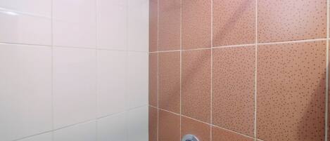 A bathroom with white and pink tiled walls, a shower area, and a visible faucet.