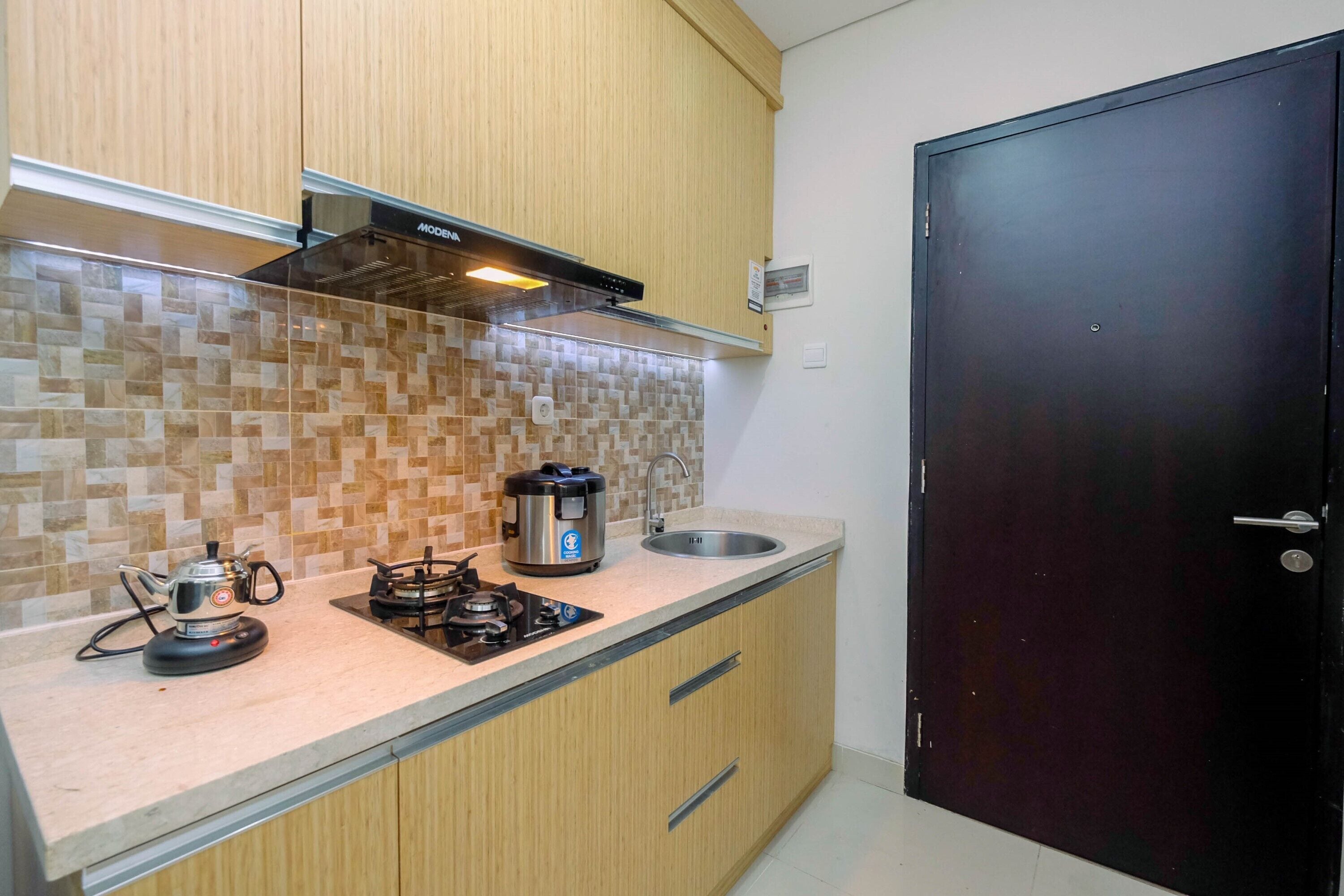 A compact kitchen with wooden cabinets, a tiled backsplash, a gas stove, a coffee maker, and a black door.