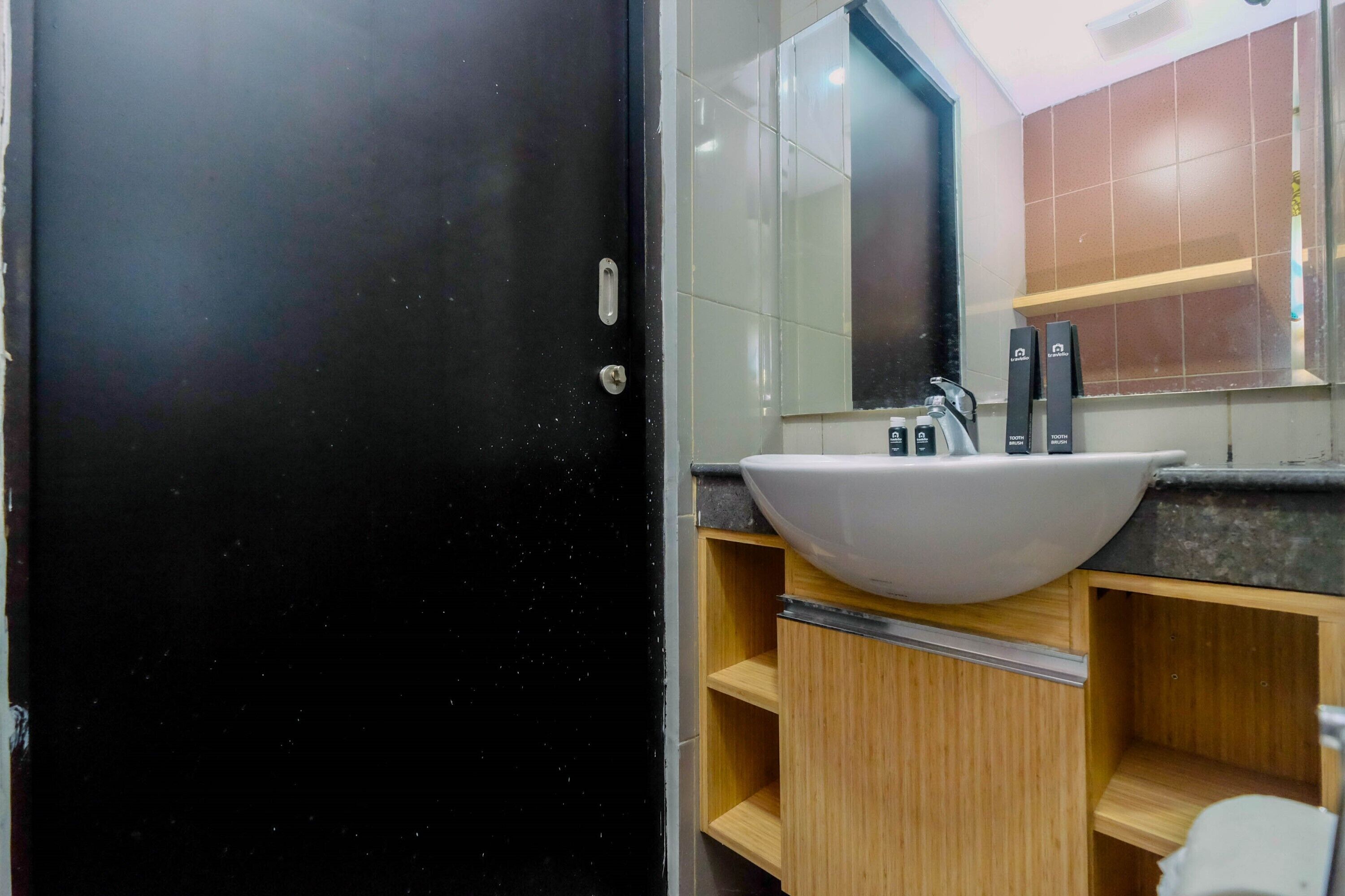A modern bathroom with a black door, a white sink, and wooden cabinets.