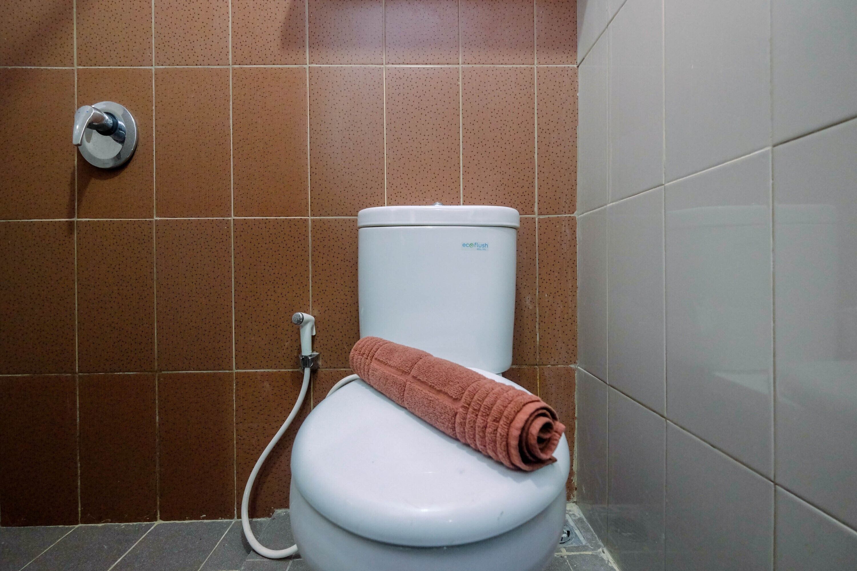 Des toilettes blanches, avec une serviette posée sur le dessus, une poignée de chasse d’eau et une tuyauterie visible.