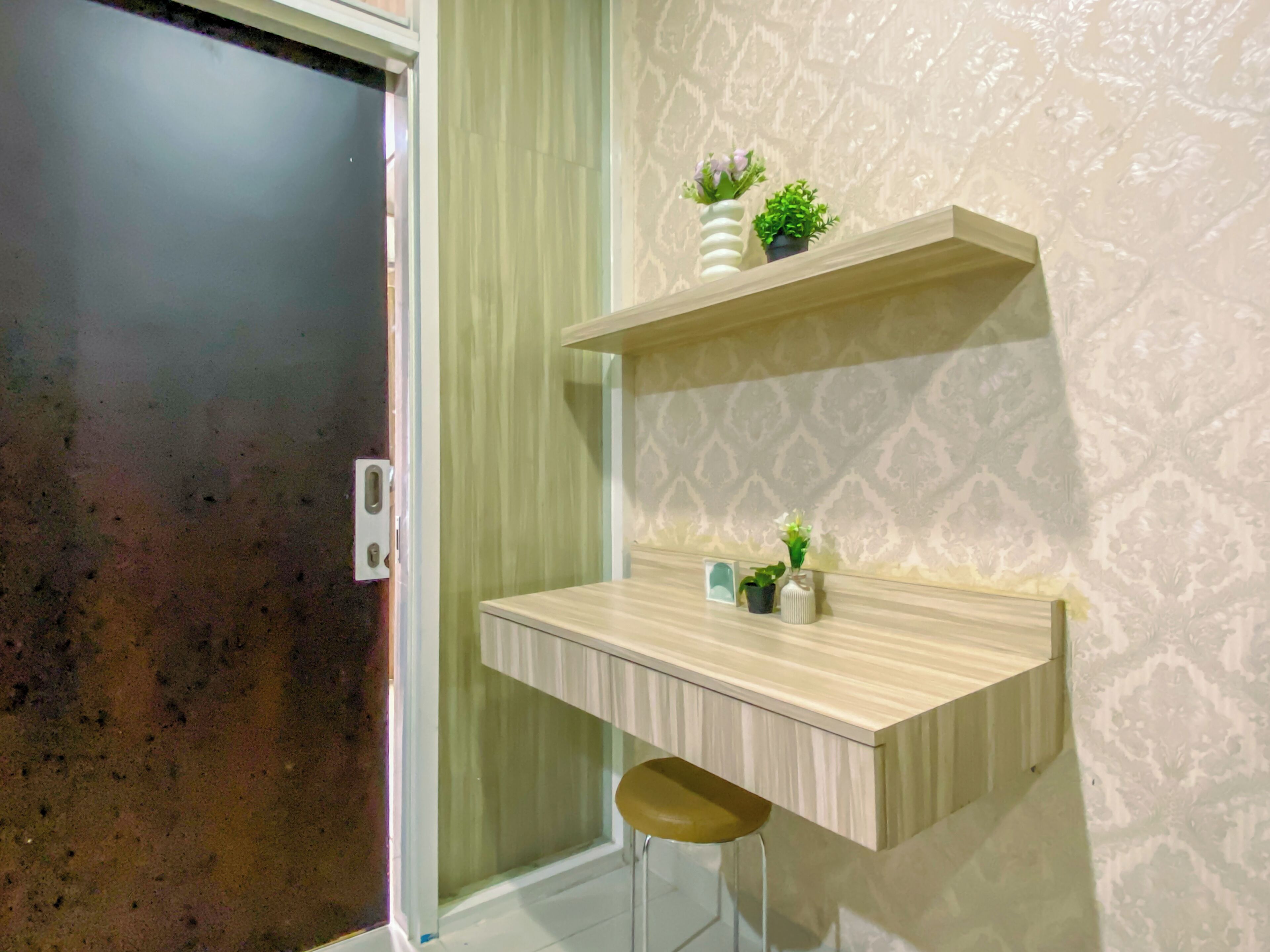 A small, modern bathroom with a wooden vanity, a stool, and decorative plants.