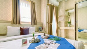 Una habitación de hotel con una cama grande, una mesita de noche con un libro y un jarrón, una ventana con cortinas y un equipo de aire acondicionado.
