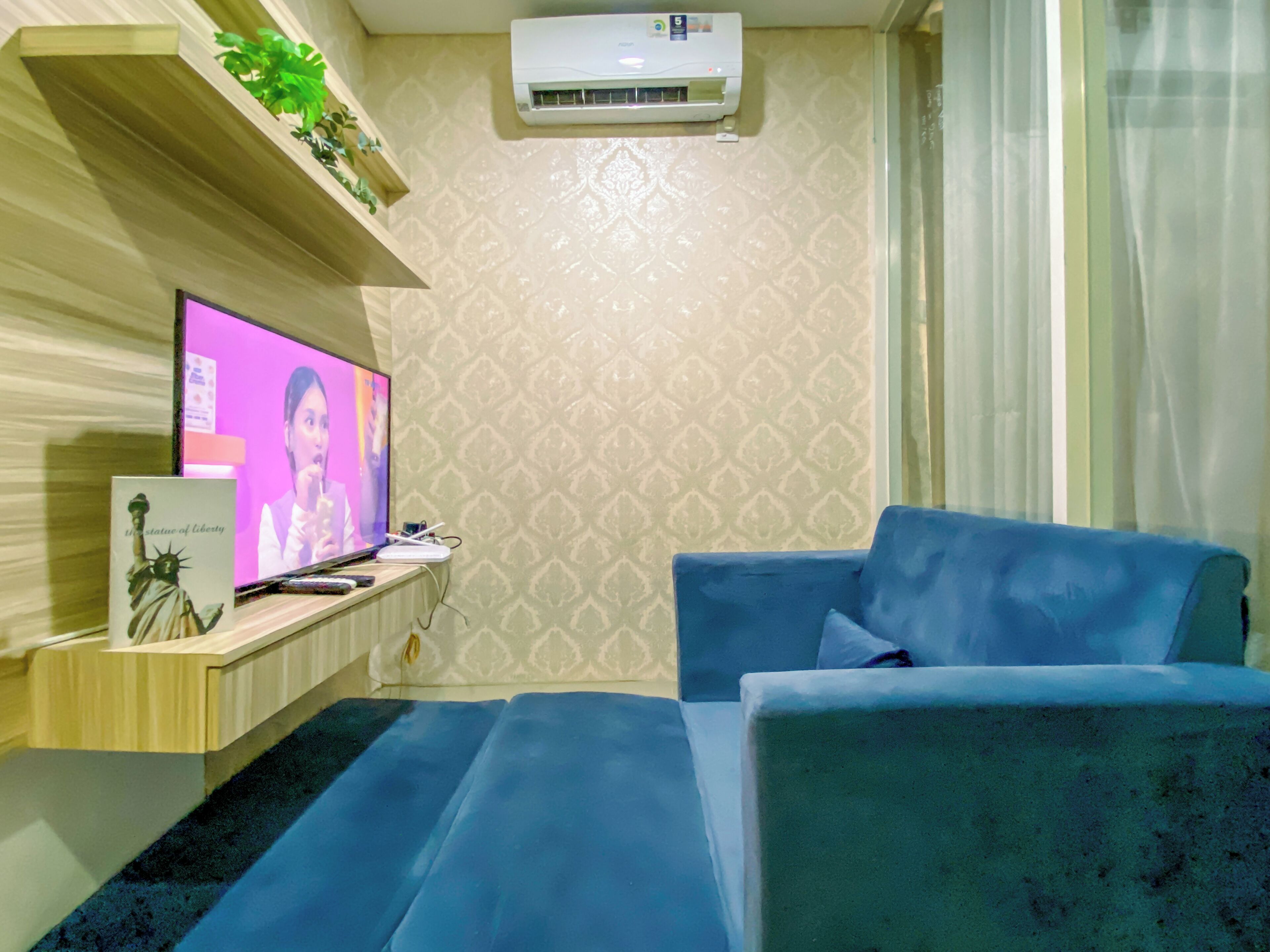 Ein Zimmer mit einem blauen Sofa, einem Fernseher auf einem Holzboden, einer Wand-Klimaanlage und Wandtapete mit Muster.