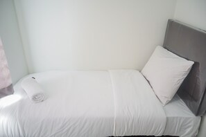 A single bed with white bedding and a grey headboard in a room with plain walls. - Comfy and Stylish 2BR Emerald Bintaro Apartment (South Tangerang)