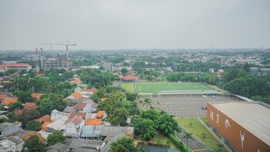 An aerial view of a cityscape with a large sports field, residential buildings, and a construction crane. - Comfy and Stylish 2BR Emerald Bintaro Apartment (South Tangerang)