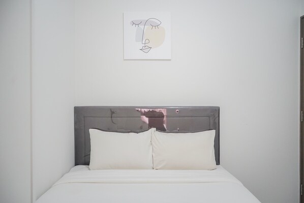 A neatly made bed with white bedding and pillows, a gray headboard, and a simple wall-mounted artwork above it. - Comfy and Stylish 2BR Emerald Bintaro Apartment (South Tangerang)