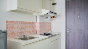 A kitchen with a sink, a stove, and a door. - Minimalist Studio Bintaro Icon Apartment near British School (South Tangerang)