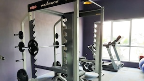 A gym with a weightlifting station, a treadmill, and a window with a view of greenery. - Minimalist Studio Bintaro Icon Apartment near British School (South Tangerang)