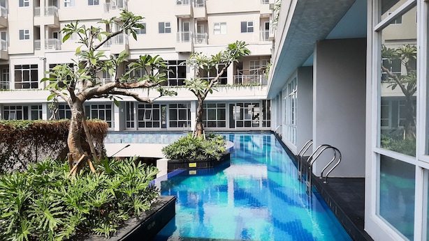 A swimming pool with a 120 cm depth, surrounded by greenery and modern buildings. - Minimalist Studio Bintaro Icon Apartment near British School (South Tangerang)