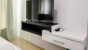 Une chambre d’hôtel moderne équipée d’un téléviseur à écran plat fixé sur un meuble blanc, d’un petit tiroir et d’une télécommande posée sur le dessus.