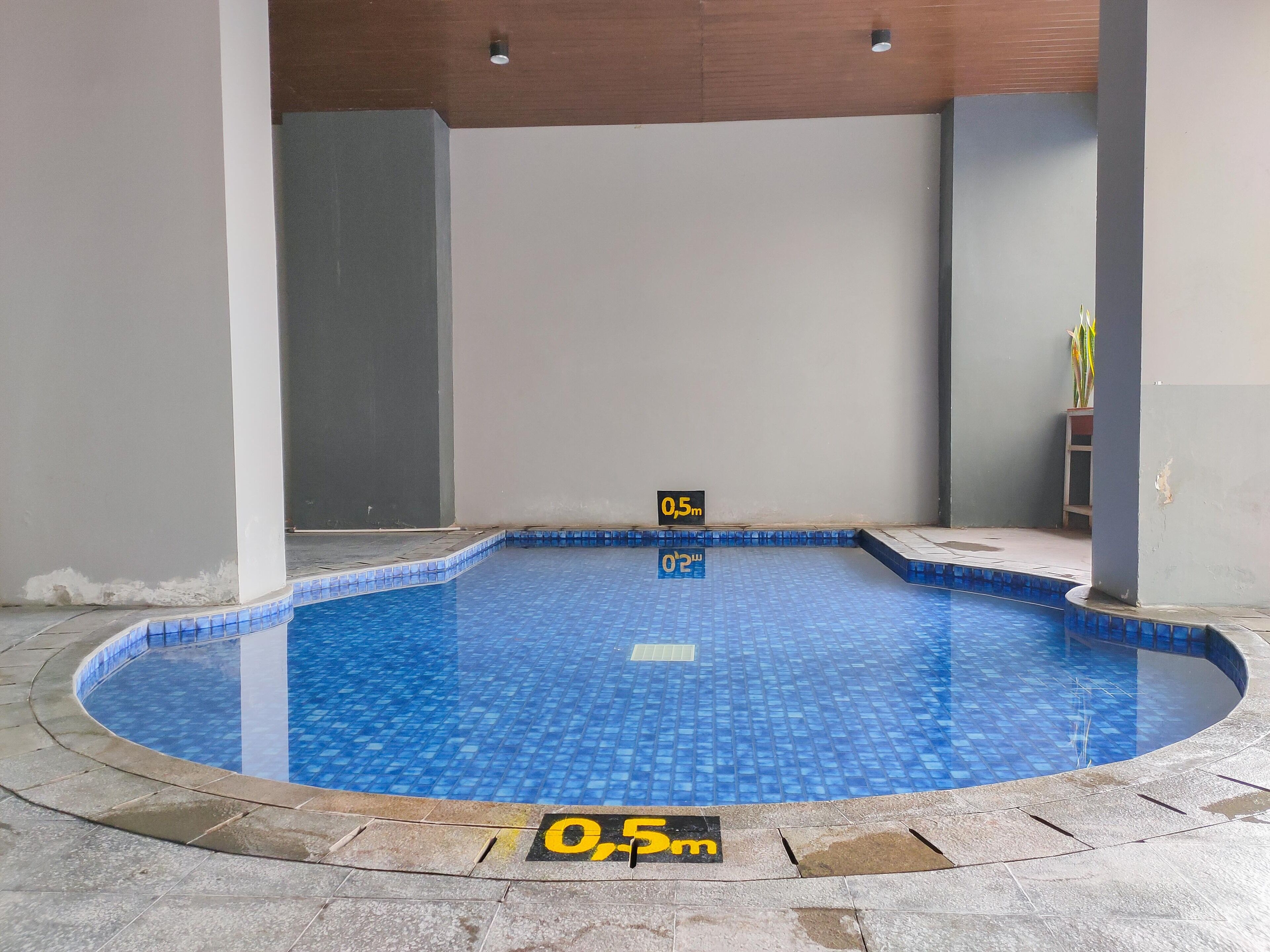 Una pequeña piscina interior con azulejos azules, rodeada de losetas de piedra y con indicaciones de profundidad.