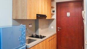 A compact kitchen with wooden cabinets, a gas stove, a blue refrigerator, and a red door. - Simply Look Studio Tamansari Mahogany Karawang Apartment (Karawang)
