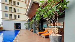 A poolside area with lounge chairs and potted plants. - Simply Look Studio Tamansari Mahogany Karawang Apartment (Karawang)