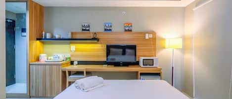 Habitación de hotel con cama, escritorio con televisor y microondas, una pequeña kitchenette y una lámpara de noche.