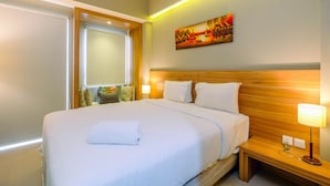 Een hotelkamer met een groot bed, houten hoofdbord, bedlampje en een schilderij aan de muur.
