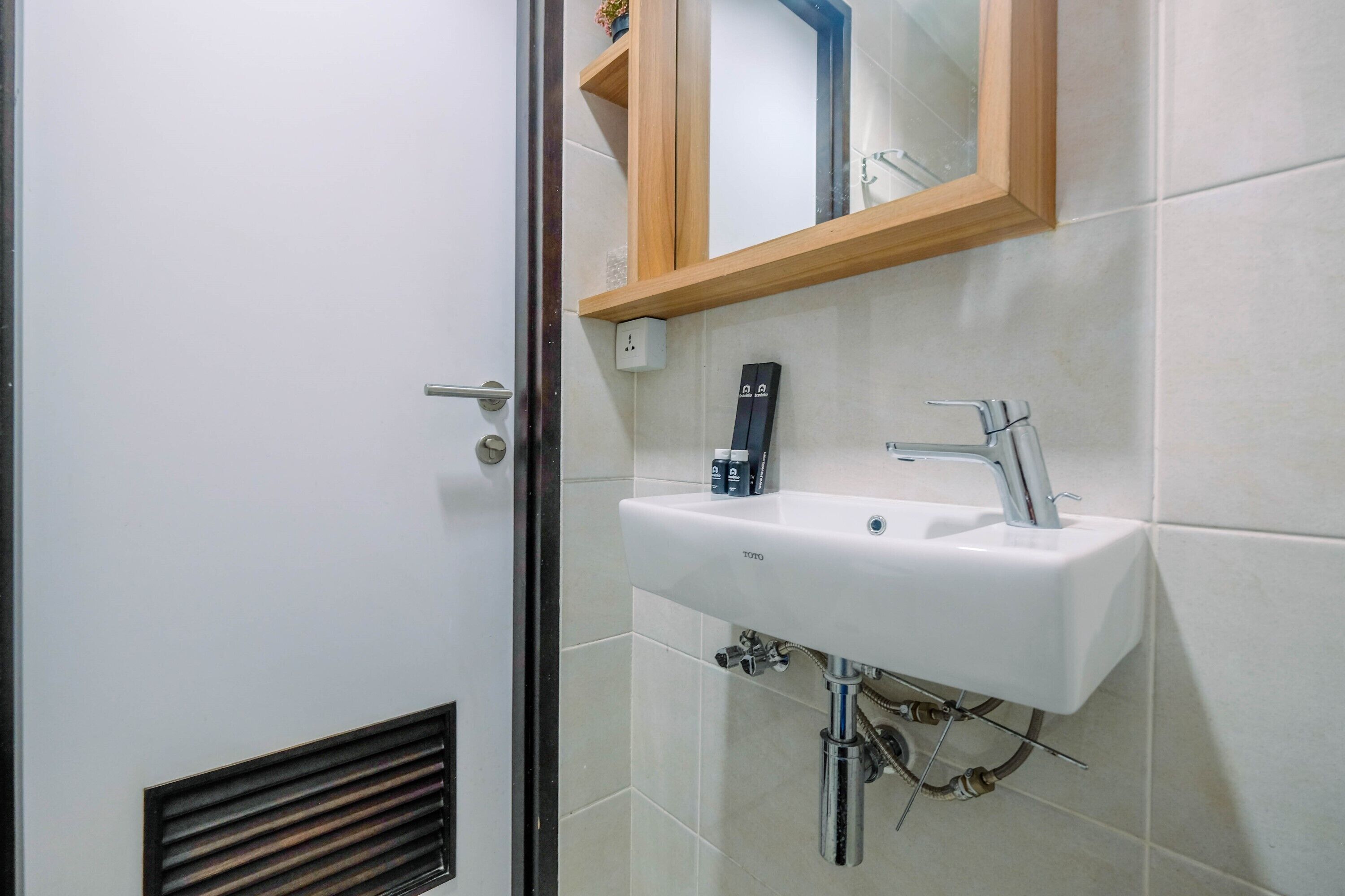 Une salle de bain avec un lavabo blanc, un miroir et une étagère en bois au-dessus du miroir.
