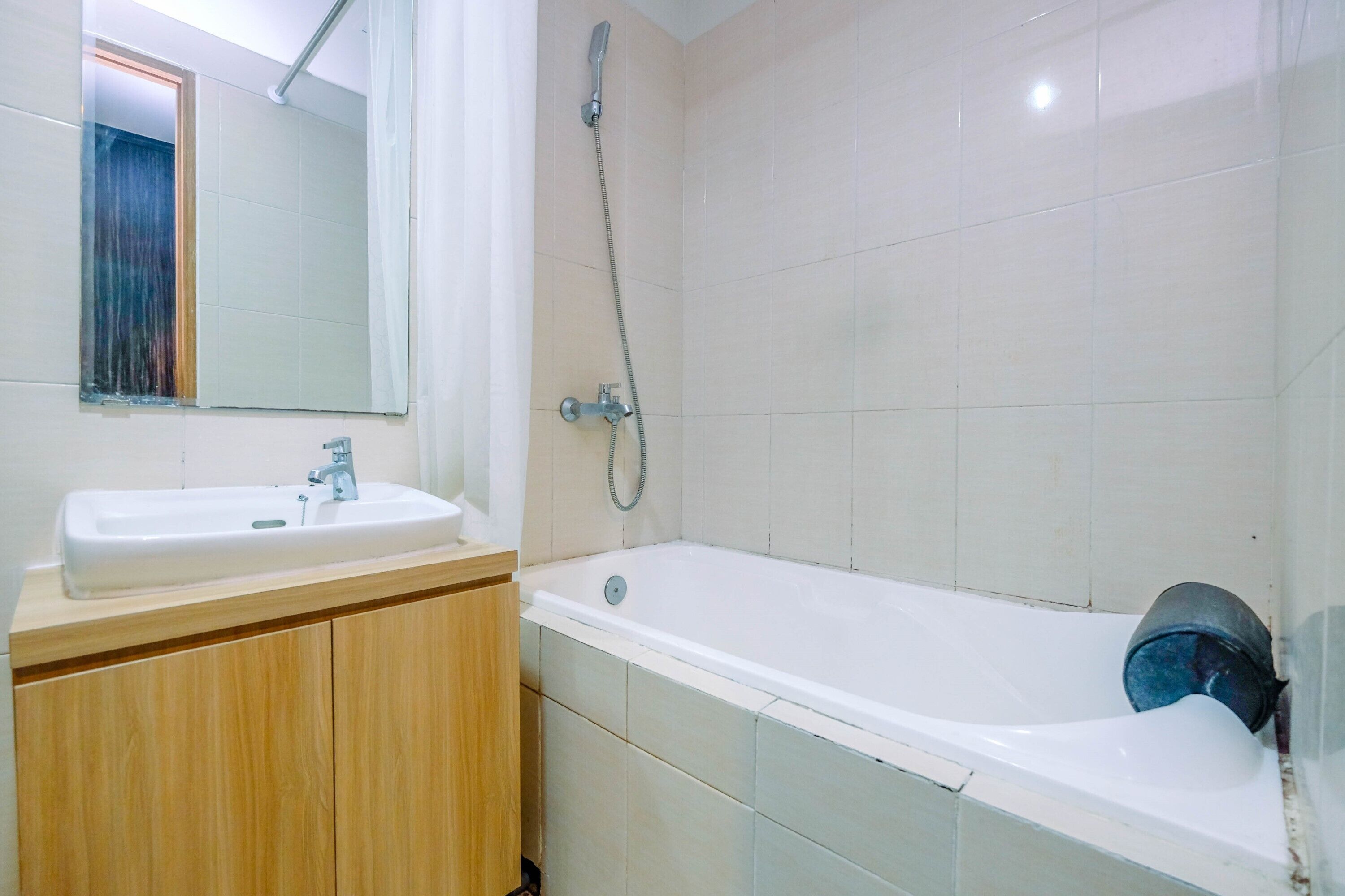 A bathroom with a white sink, wooden vanity, a mirror, and a white bathtub with a showerhead.