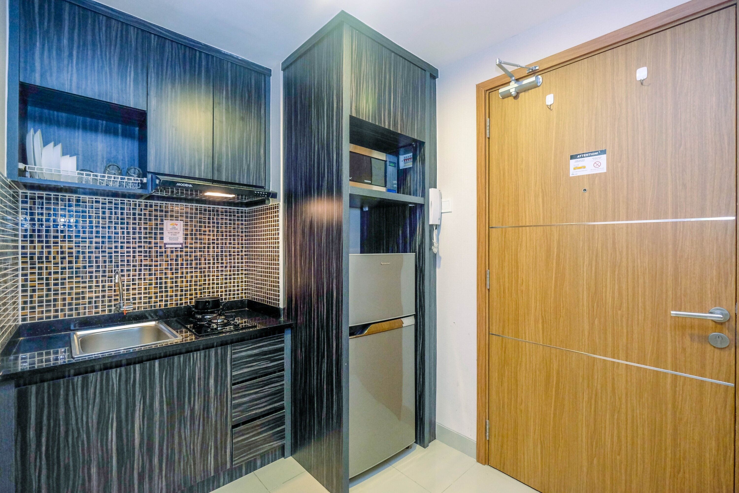 Una cocina moderna con microondas incorporado, un fregadero y un refrigerador. A la derecha, una puerta de madera.