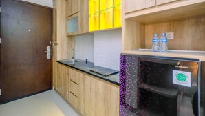 A compact kitchen with wooden cabinets, a black countertop, and a stainless steel refrigerator. - Minimalist Mustika Golf Residence Studio Apartment with City View (Cikarang)