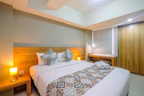 Hotellihuone, jossa on suuri sänky, puinen pääty, kuviollinen päiväpeite, kaksi yöpöytälamppua, yöpöytä ja puinen vaatekaappi.