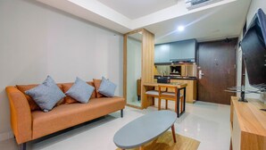 A compact living space with a sofa, a small table, a kitchen area, and a TV. - Comfortable 1BR Apartment at Mustika Golf Residence (Cikarang)