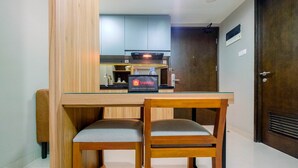 A compact kitchen with a wooden table and two chairs, a refrigerator, and a travelello sign indicating food and beverage services. - Comfortable 1BR Apartment at Mustika Golf Residence (Cikarang)