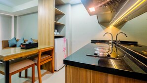 A compact kitchen with a dining area, wooden cabinets, a refrigerator, and a black countertop. - Comfortable 1BR Apartment at Mustika Golf Residence (Cikarang)
