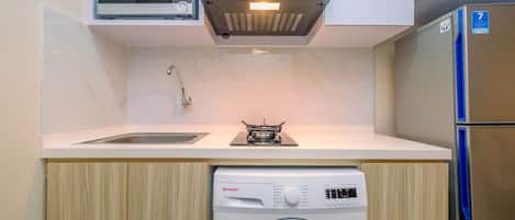 A compact kitchen with a microwave, stove, sink, and washing machine.