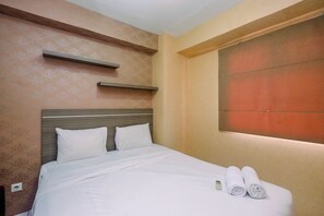 A neatly made bed with white linens and pillows, a bedside table with a power outlet, and a wall-mounted shelf above it. - Strategic and Homey 1BR Kalibata City Apartment (Jakarta)