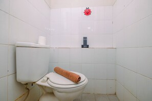 A small, white-tiled bathroom with a toilet, a toilet paper holder, and a towel on the seat. - Strategic and Homey 1BR Kalibata City Apartment (Jakarta)
