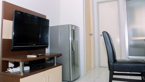 A kitchenette with a flat-screen TV, a stainless steel refrigerator, and a black leather chair. - Compact and Cozy 2BR Kalibata City Apartment (Jakarta)