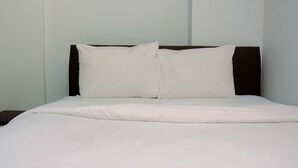 A neatly made bed with white bedding and a dark headboard in a room with plain walls. - Compact and Cozy 2BR Kalibata City Apartment (Jakarta)