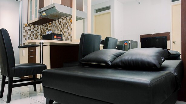A compact room with a sofa, a desk, a chair, a television, and a kitchenette. - Compact and Cozy 2BR Kalibata City Apartment (Jakarta)