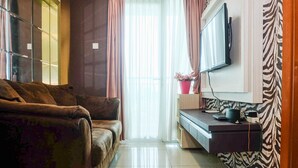 A living room with a sofa, a TV mounted on the wall, a desk with a computer, and a window with curtains.