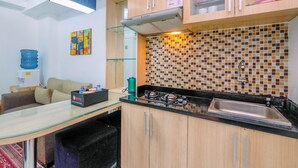 A compact kitchen with a gas stove, a sink, and a microwave. There is a glass table with a box on it, and a colorful abstract painting on the wall.