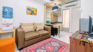A compact living space with a sofa, a water dispenser, a colorful artwork, a kitchen area, and a television.