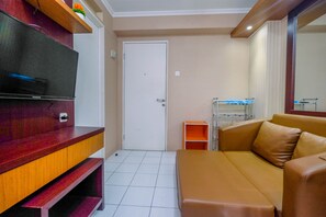 A living room with a TV, a sofa, a wooden entertainment unit, and a door. - Minimalist 2BR Apartment at Kalibata City near Shopping Center (Jakarta)