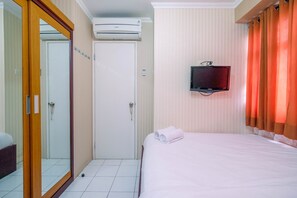 A hotel room with a bed, a television mounted on the wall, an air conditioning unit, and a sliding door. - Minimalist 2BR Apartment at Kalibata City near Shopping Center (Jakarta)